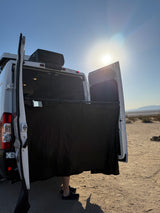 RV rental camper van with open rear doors and a black privacy curtain setup for outdoor showering/changing in the desert.
