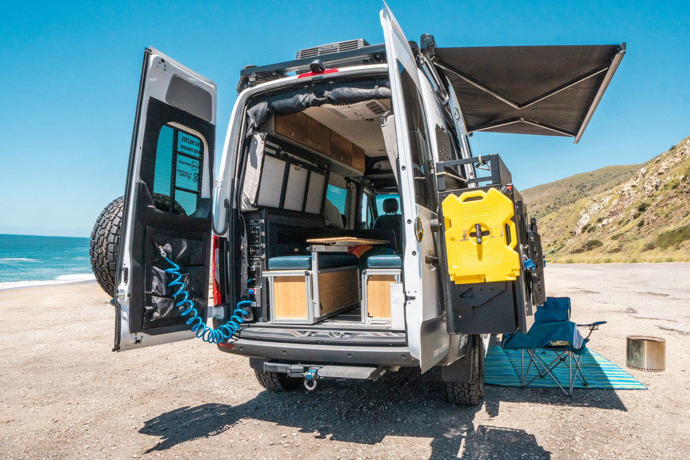 RV rental with open rear doors by the beach, showcasing its adventure-ready interior, gear, and deployed awning. — photo 11
