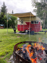 Enjoy a relaxing campout! This RV rental has an awning, comfy chairs, and a warm fire pit in a lush green setting.