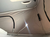 Interior of an RV rental camper van, showing a beige pop-top roof, a bright flexible USB LED light, and the grey vehicle ceiling with a grab handle.