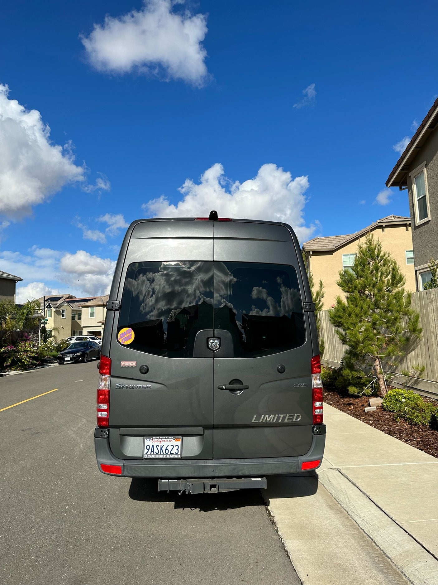 Rear view of a gray Winnebago Sprinter RV rental parked on a sunny California residential street.