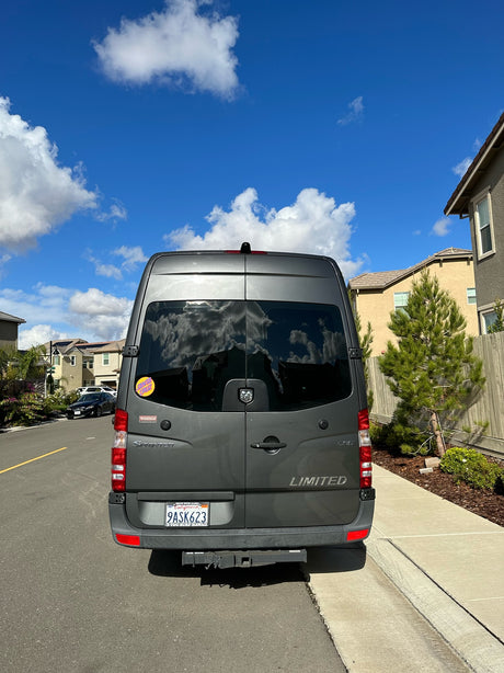 Rear view of a gray Winnebago Sprinter RV rental parked on a sunny California residential street.