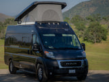 An rv rental: a dark Winnebago Solis camper van with pop-top extended, parked in a scenic outdoor setting.