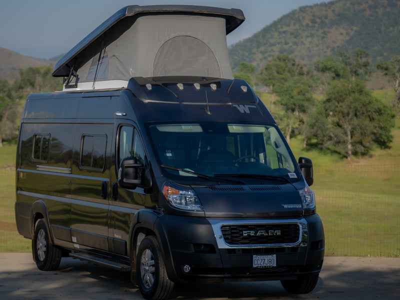 An rv rental: a dark Winnebago Solis camper van with pop-top extended, parked in a scenic outdoor setting. — photo 7