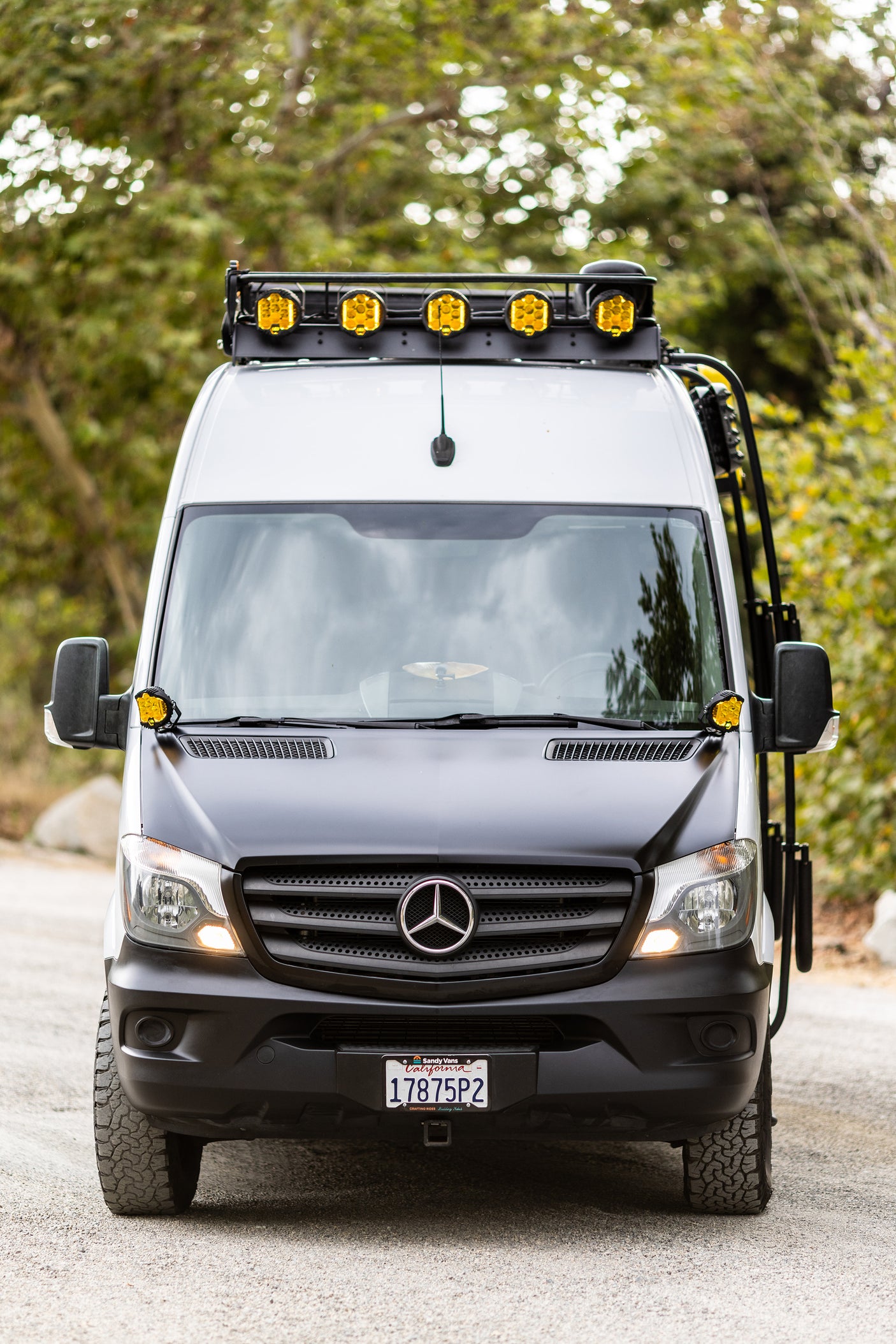 Front-facing white & black custom Mercedes Sprinter van, with off-road lights and tires. Ideal for RV rental.