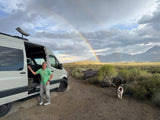 Enjoy your RV rental adventure! Man and dog with a Starlink-equipped van under a rainbow in a scenic landscape.