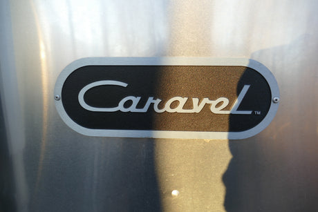 Silver 'Caravel'™ emblem on a black plaque, riveted to a brushed aluminum Airstream travel trailer, ideal for rv rental.