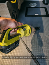 Inside an RV rental, a hand uses a Ryobi cordless handheld vacuum on the gray textured floor. Cleaning convenience included for trips.