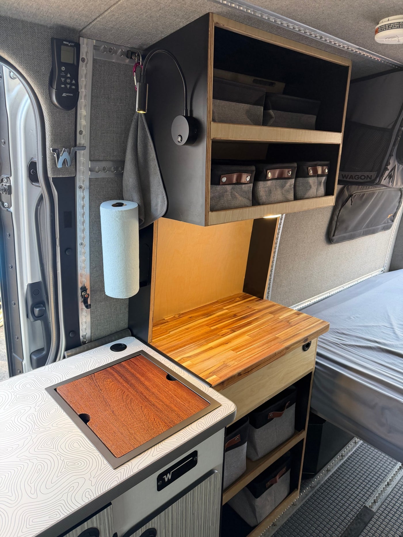 Compact rv rental camper van interior: kitchen area with wood countertop cover, overhead storage, and bed visible on the right. — photo 6