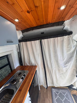 Step inside this RV rental van! View a sleek kitchen with stove/sink, warm wooden ceiling, and a full-height divider curtain.