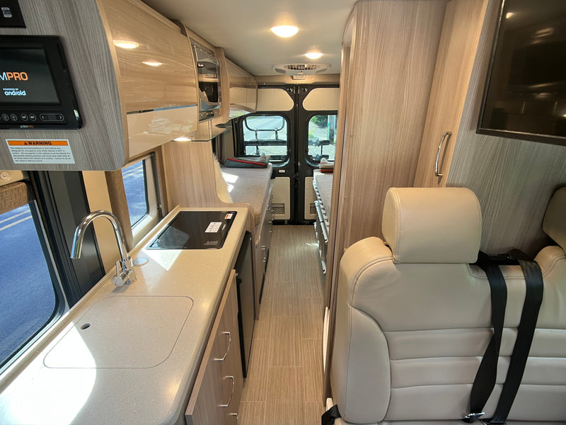 A narrow view inside an RV rental, showcasing its compact kitchenette, overhead storage, and versatile seating. — photo 7