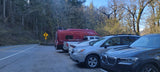 Red RV rental and cars parked in a forest parking lot beside a winding road with a 25 mph sign.