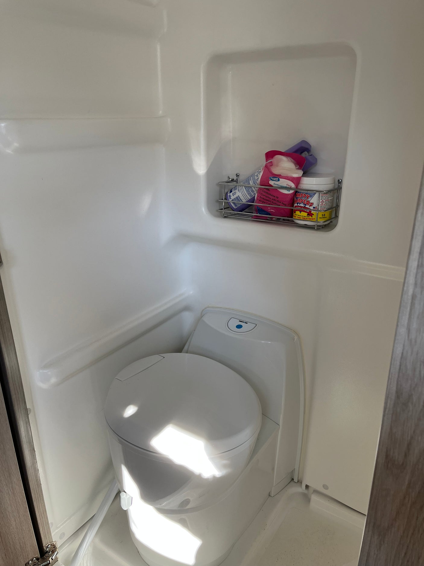 Inside an RV rental: a compact white bathroom featuring a modern toilet and a shelf with RV toilet tank treatment.