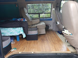 RV rental interior: A cozy, converted van living space featuring a bed, tan seats, and wood flooring.