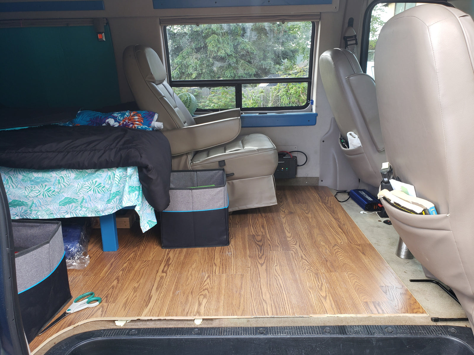 RV rental interior: A cozy, converted van living space featuring a bed, tan seats, and wood flooring.