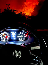 Intense distant fire lights up the night sky, viewed from a Ram RV rental. Dashboard glows in the foreground.