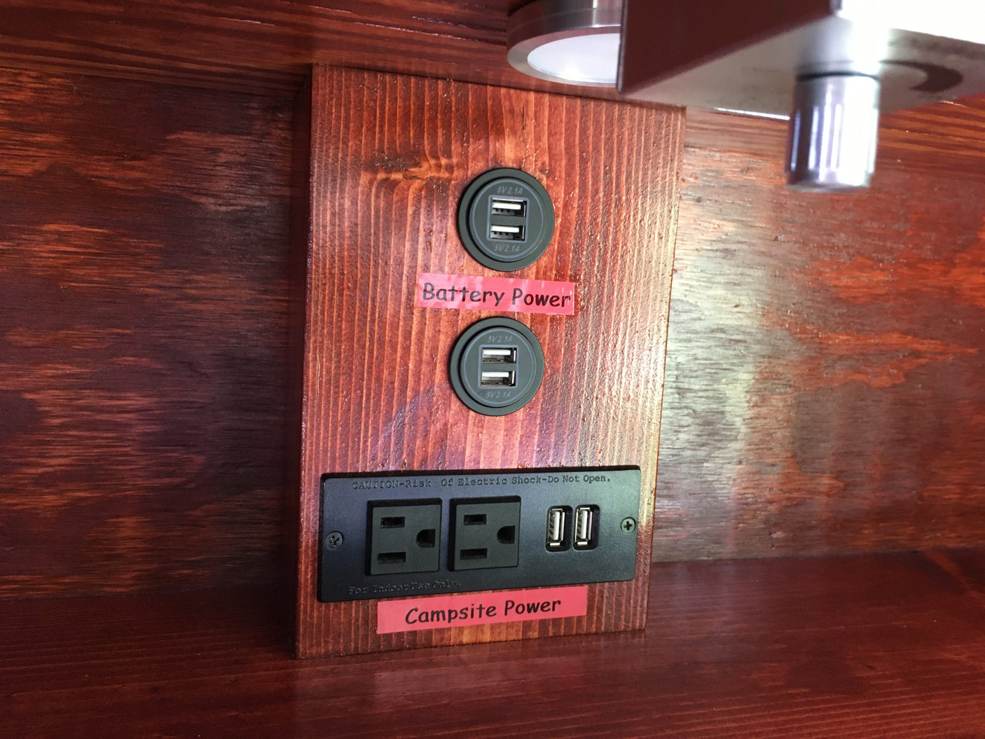 RV rental power station: Wooden panel with USB ports (battery) & AC/USB outlets (campsite power) for charging devices.