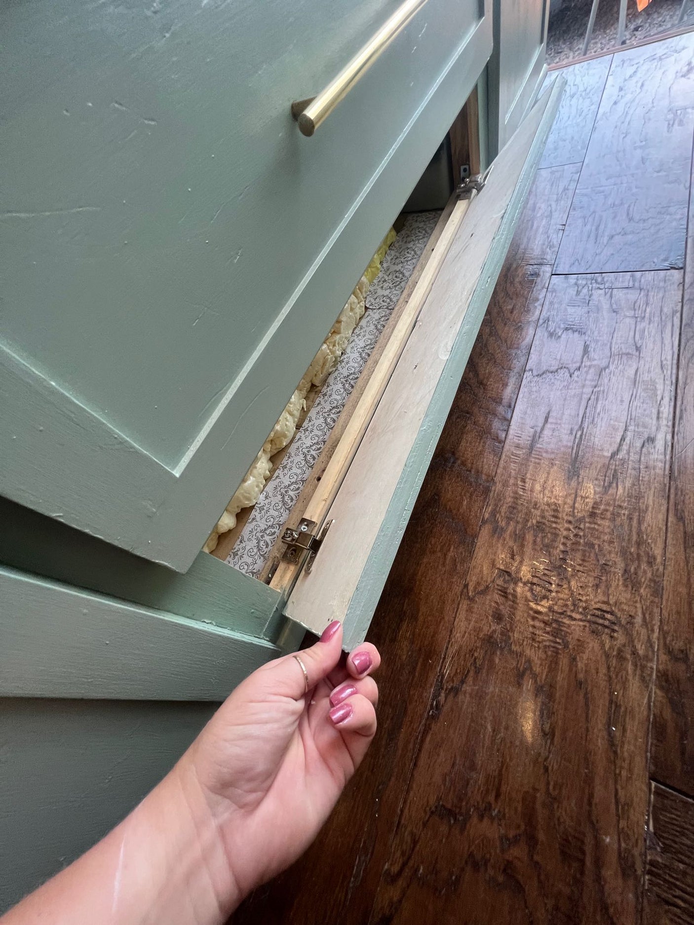 A hand opens a hidden cabinet panel in an RV rental, revealing foam insulation & patterned lining.