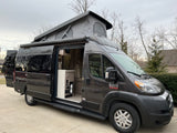 Experience adventure! This modern grey pop-top camper van RV rental features an open side door, spacious interior, and rear bike rack.