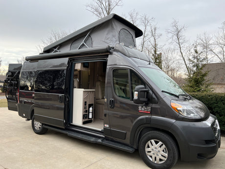 Experience adventure! This modern grey pop-top camper van RV rental features an open side door, spacious interior, and rear bike rack.
