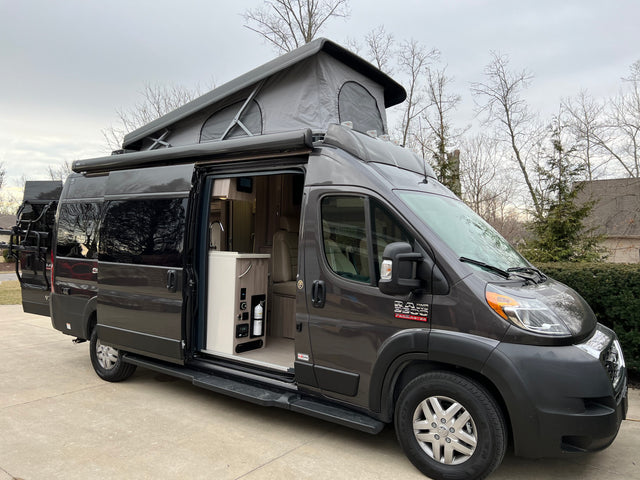 Experience adventure! This modern grey pop-top camper van RV rental features an open side door, spacious interior, and rear bike rack.
