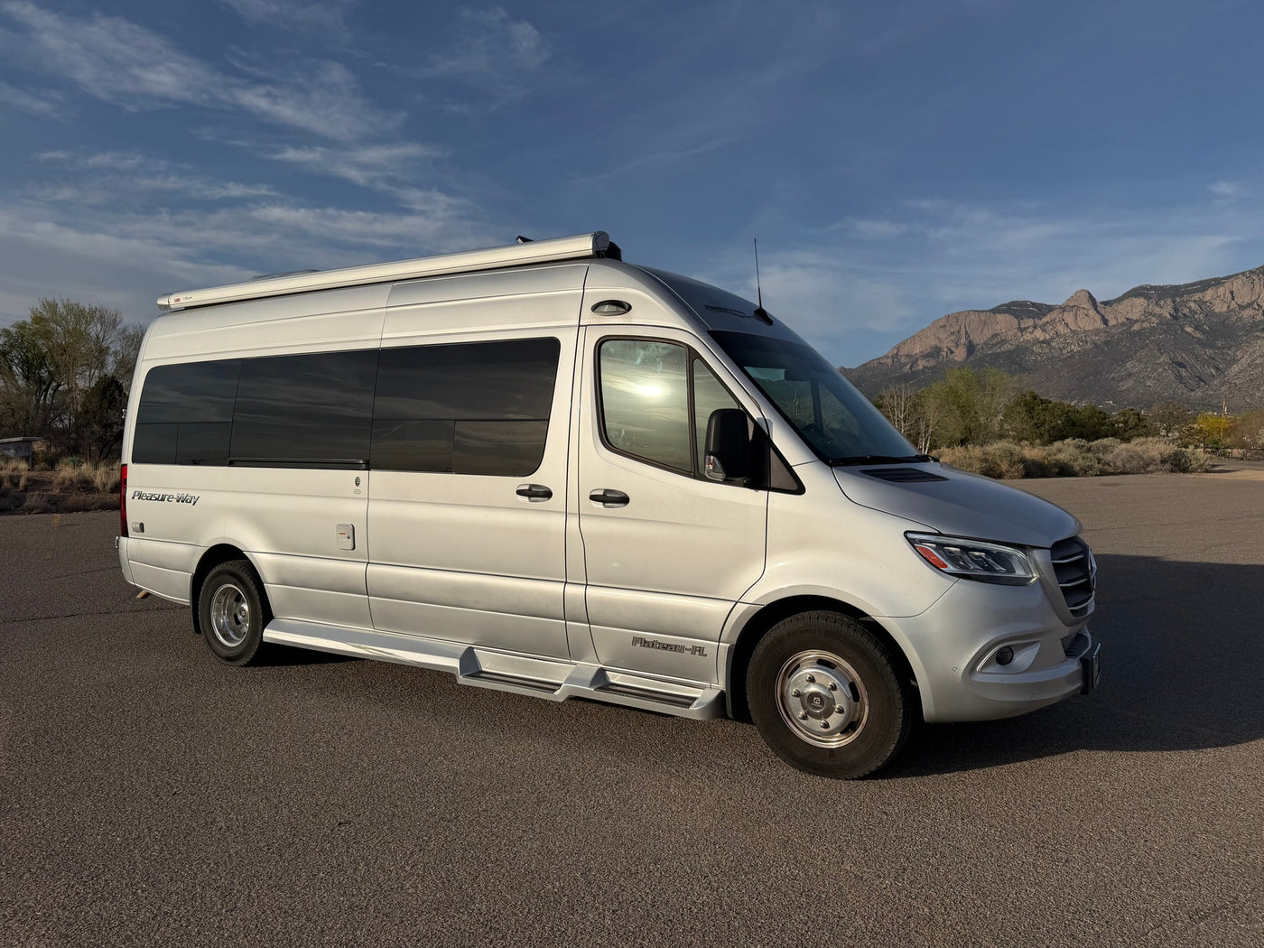 Silver Pleasure-Way rv rental van parked on asphalt, mountains and blue sky in background. — photo 3