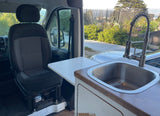 RV rental interior: passenger seat, small table, and a kitchen sink with modern faucet. Street view visible outside.