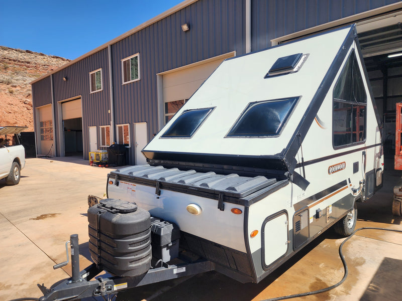 This Rockwood A-frame rv rental camper awaits adventure, parked by a shop with desert hills behind it. — photo 4
