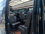 Interior of a luxury RV rental van with black quilted leather captain's chairs, wood floor, and overhead lighting.
