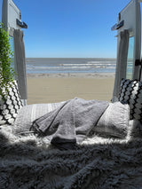 Perfect RV rental view: sunny beach & ocean from a cozy interior. Pillows, blankets, and faux fur invite relaxation.