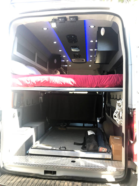 RV rental: Inside a custom camper van conversion with a comfortable sleeping area, compact kitchenette, and vibrant LED lighting.