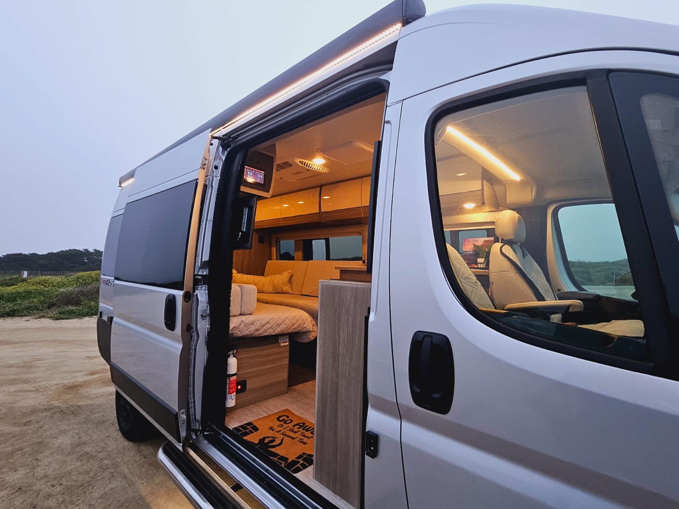  rocky coast overlooking the ocean with waves and a bench.|Silver camper van RV rental parked at dusk with an open door — photo 4