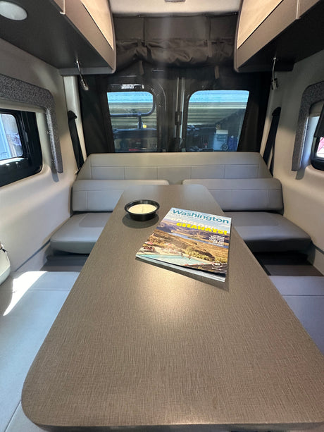 Comfortable RV rental dining area with gray benches, a table, and a "Washington" travel guide, inviting adventure.