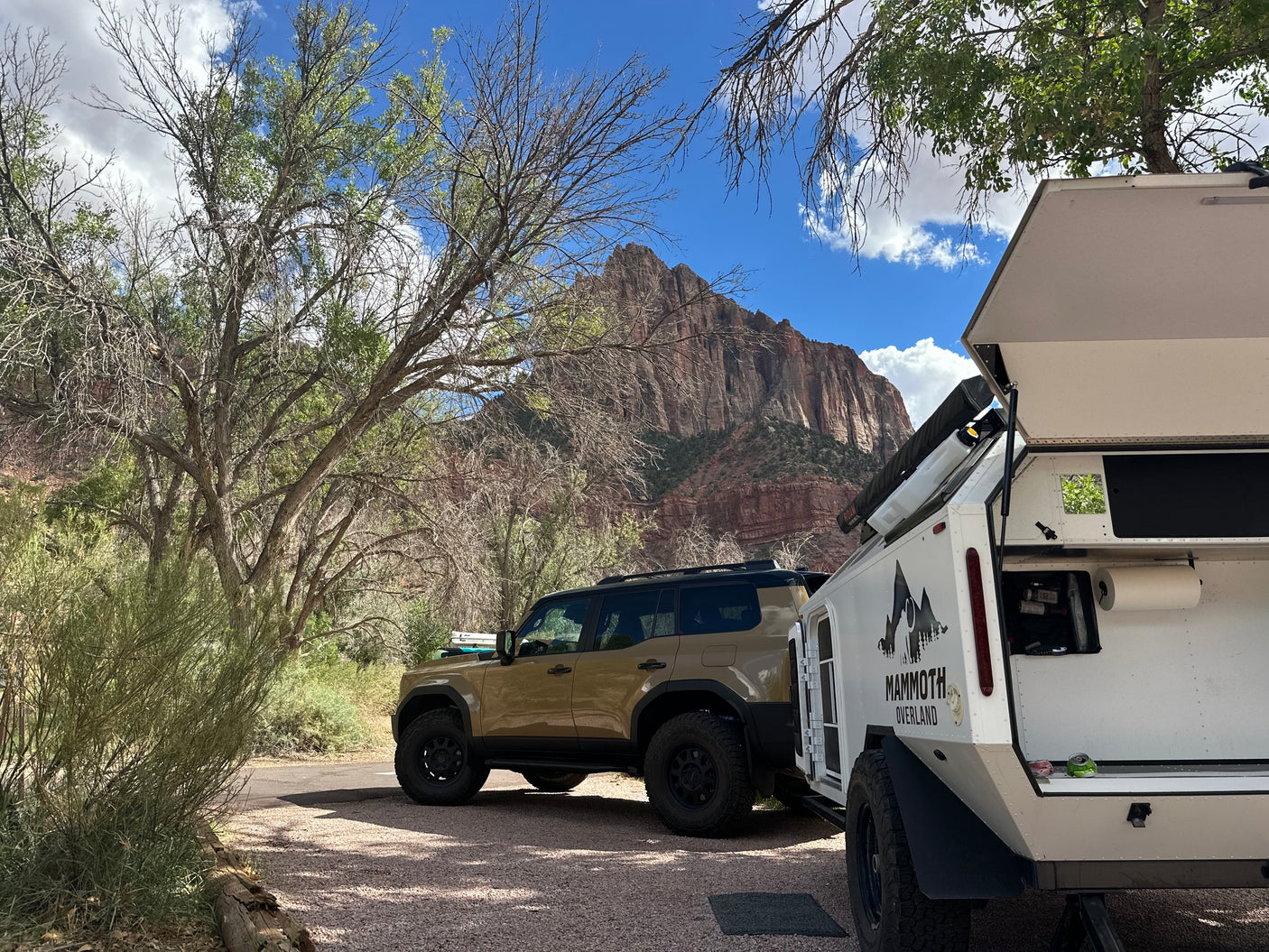 Adventure-ready RV rental setup: Tan SUV and Mammoth Overland trailer at a scenic mountain campsite, perfect for outdoor travel.