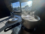 Cooking inside an RV rental! Steaming pot of boiling water, non-alcoholic Blue Moon can, and a sunny outdoor view.