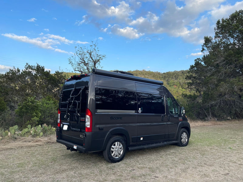 Dark grey Scope camper van parked in a grassy field with trees under a blue sky, perfect for your next rv rental adventure. — photo 2