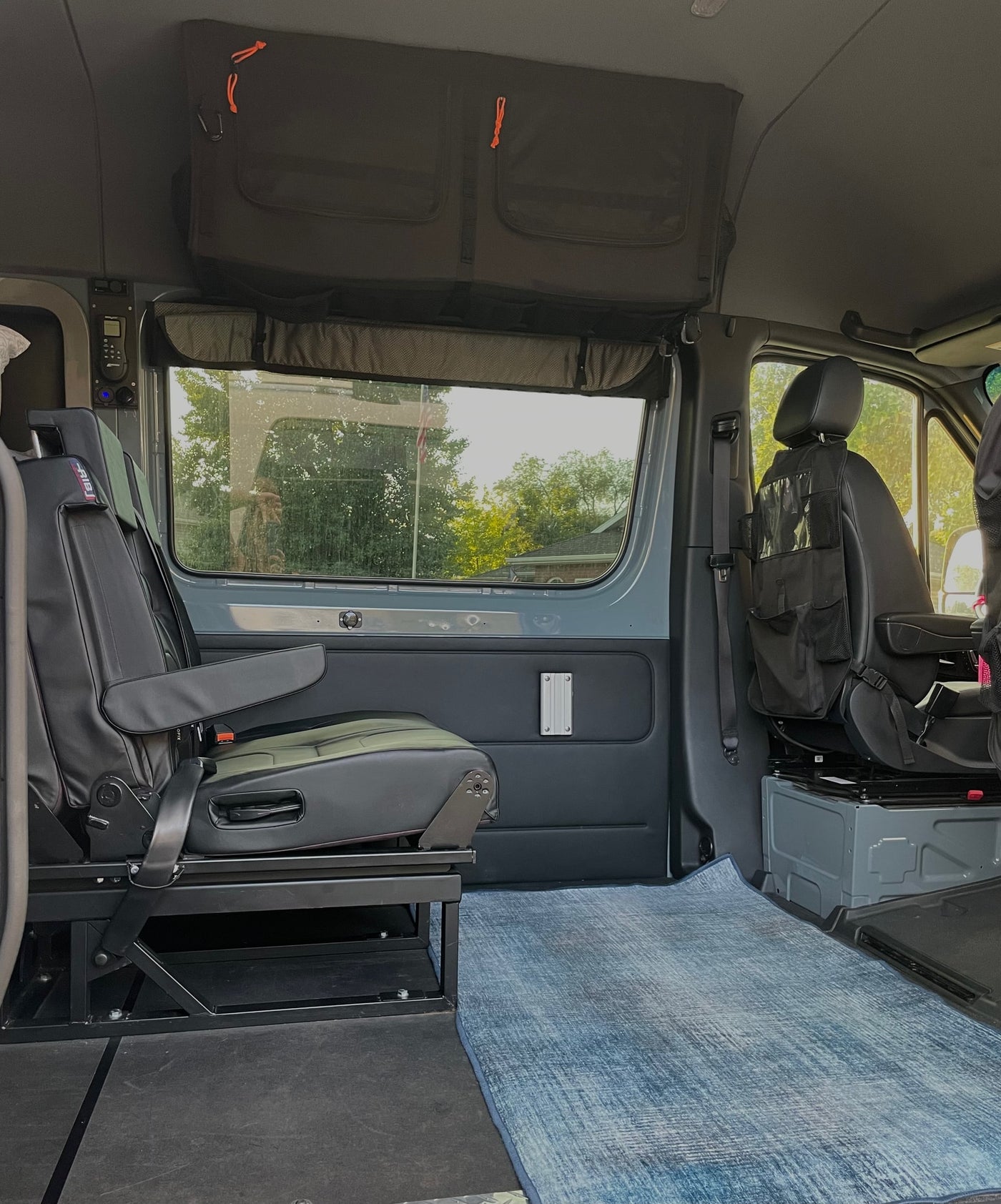 RV rental interior: View of a practical camper van space with modular seating, overhead storage, and textured blue flooring. — photo 7