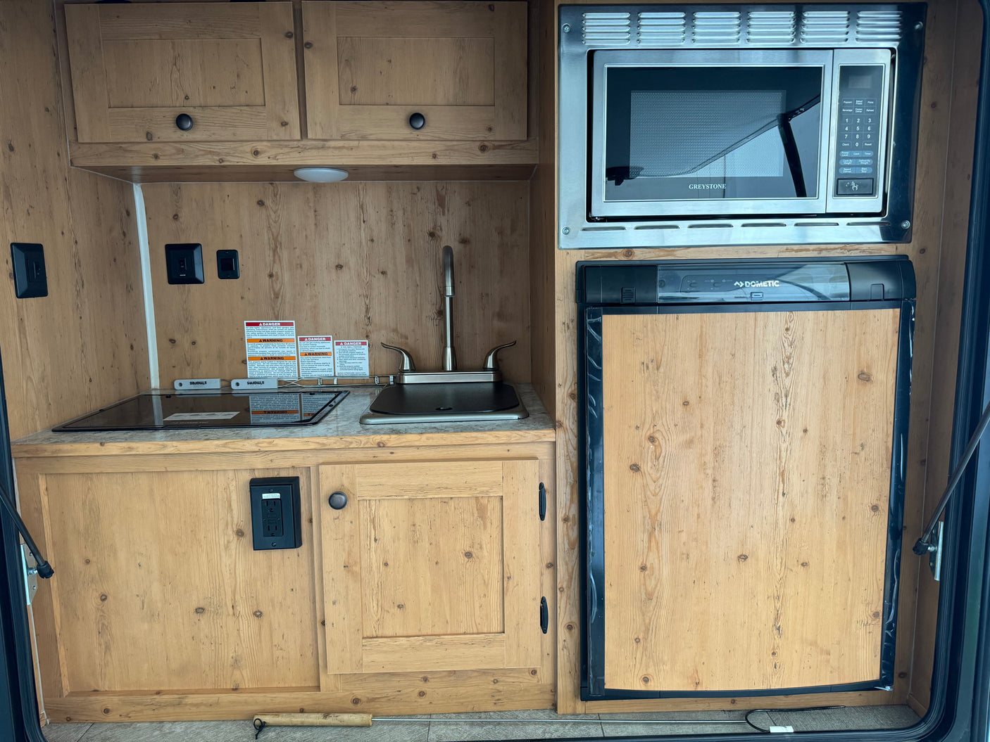RV rental kitchen: Features a sink, electric cooktop, Greystone microwave, Dometic fridge, and light wood cabinetry.