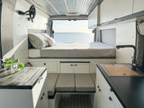 Spacious RV rental interior with a cozy bed, ocean view, modern kitchen, and comfortable living area.