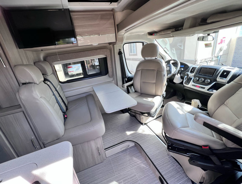 RV rental interior: light-toned seating, versatile table, TV, and driver's cockpit for comfortable travel. — photo 8