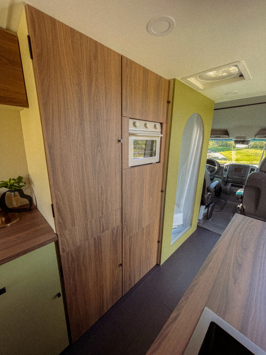 RV rental: Modern camper van interior with custom wood cabinetry, built-in oven, and a stylish green partition leading to the driver's cab.