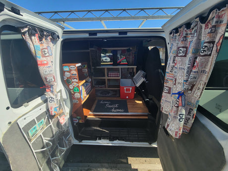 This compact rv rental camper van interior is set up for a comfy road trip, featuring custom storage and Route 66 curtains.