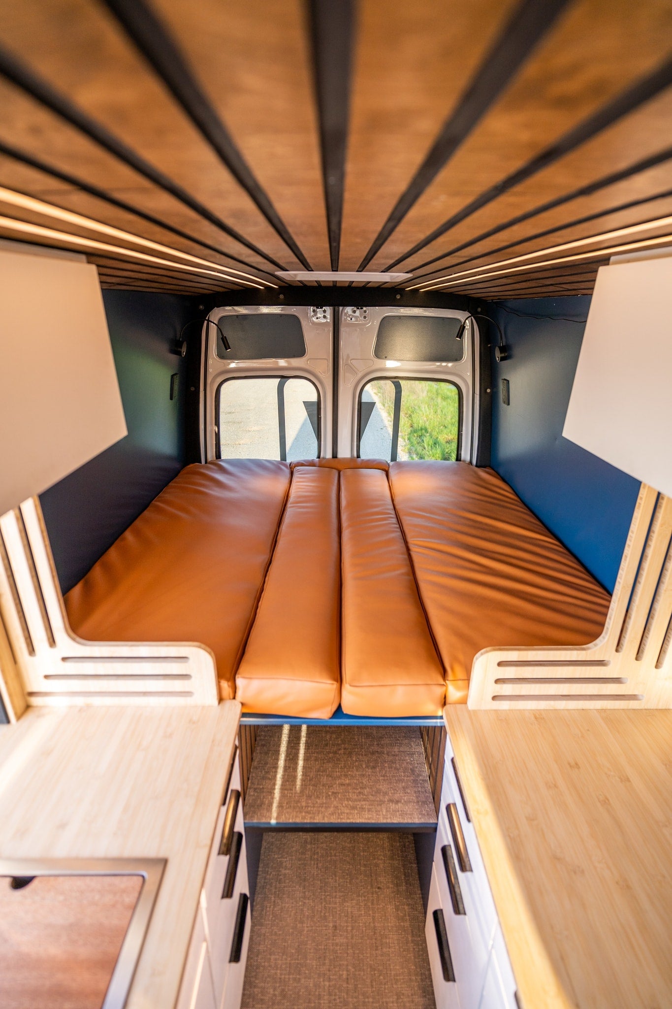 An inviting rv rental interior with a slatted wooden ceiling, warm lighting, a plush brown bed, and light wood storage cabinets. — photo 4