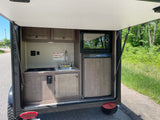 Compact RV rental kitchen with sink, stovetop, microwave, and fridge, perfect for camping adventures.