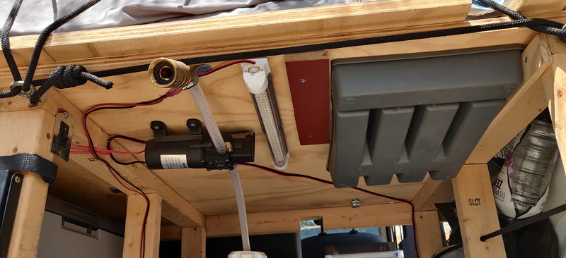 Underneath an RV rental setup: a 12V water pump, clear tubing, wiring, LED lights, and storage optimizing mobile living. — photo 5