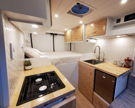 Clean, bright rv rental interior with a fully equipped kitchen (stove, sink, fridge), cozy bed, and storage cabinets.