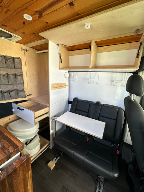 This RV rental's cozy interior features a wooden ceiling, smart storage, compact toilet, dinette, and comfy seating for adventure.
