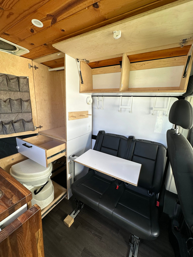 This RV rental's cozy interior features a wooden ceiling, smart storage, compact toilet, dinette, and comfy seating for adventure. — photo 12