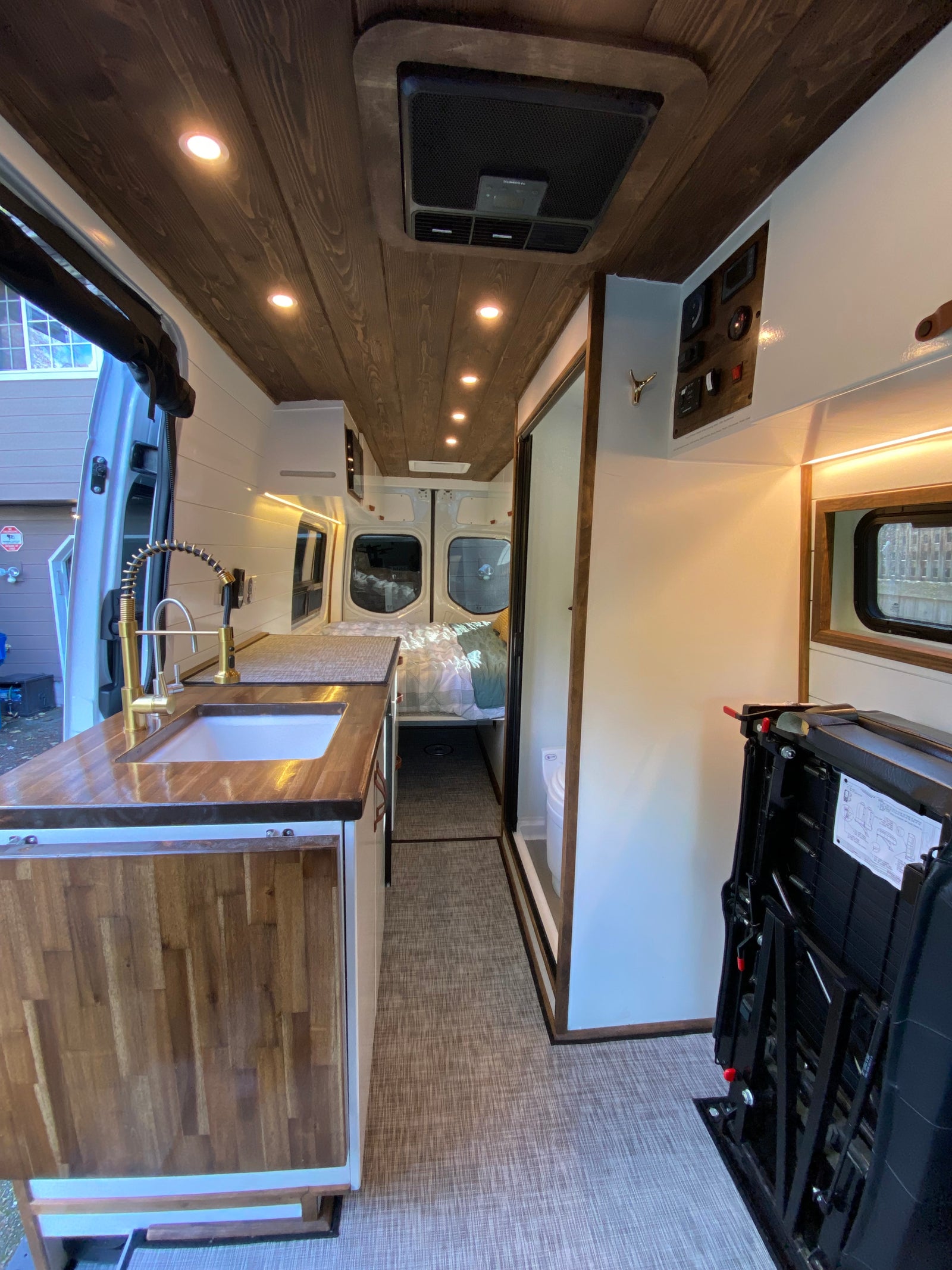 A modern RV rental interior: featuring a well-appointed kitchen with gold fixtures, wood ceiling, bed, and cozy living space.