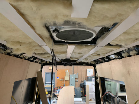 Inside an RV rental van conversion: Ceiling insulation and fan installed. Plywood paneling in progress for the interior build.